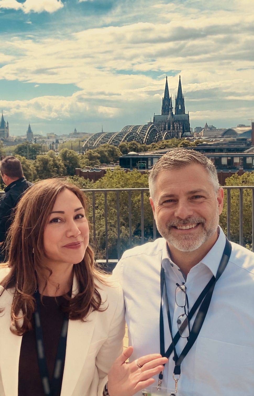 Founder Dela Kunzmann with a colleague on a rooftop terrace in Cologne, with the cathedral and the Hohenzollern Bridge behind them.